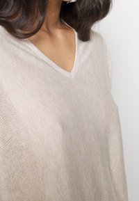 Jasnobeżowy sweter dzianinowy z dekoltem w serek, wykonany z miękkiej, teksturowanej tkaniny z subtelnymi prążkami na krawędziach.