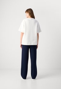 White oversized t-shirt with short sleeves paired with navy wide-leg trousers, featuring a smooth texture and minimalistic design.
