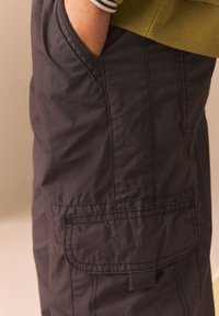 Pantalones cortos cargo negros hechos de una tela ligera, con bolsillos laterales, costuras visibles y un ajuste relajado.