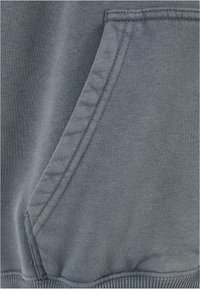 Grå sweatshirt stof med en kængurulomme. Glat tekstur med en veldefineret søm og ribbestrikket kant, der fremhæver holdbare syninger.