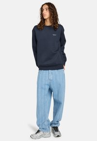 Felpa navy con collo a giro, polsini a costine e dettagli del logo. Abbinata a jeans oversize azzurri con motivi verticali e sneakers.
