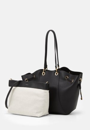 Zwarte getextureerde leren tas met gouden oogjes en handvatten, vergezeld van een kleinere witte stoffen pouch met zwarte rand en band.
