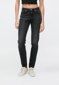 Čierne priliehavé rifle s vysokým pásom, piatimi vreckami, jemným prešitím a hladkou textúrou, kombinované so svetlými teniskami.