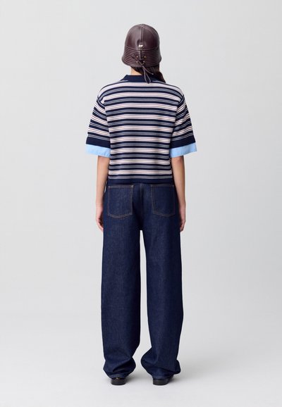 Top de manga corta a rayas en azul marino, crema y azul claro; combinado con jeans de pierna ancha en denim oscuro; textura suave; detalles mínimos.