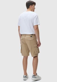 Beige cargo shorts med flere lommer, laget av lett stoff. Kombinert med en ensfarget hvit t-skjorte og grå sportssko.