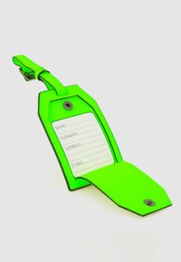 Neon groene bagagelabel met een achthoekige vorm, voorzien van een witte binnenkaart voor contactgegevens, vastgehouden door een metalen drukknoopsluiting.