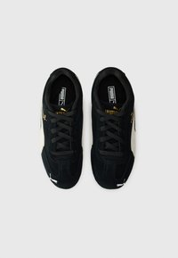 Baskets en daim noir avec des accents beiges, bout rond, surface texturée, lacets plats et détail de logo doré sur le côté.