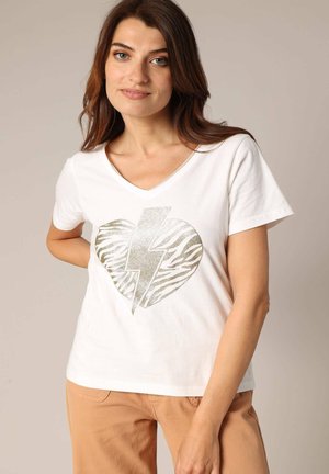 T-shirt blanc en coton avec un col en V, présentant un cœur en motif zèbre doré métallique et un graphique d'éclair à l'avant.