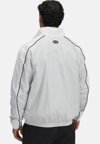 Witte jas met zwarte zijaccenten, elastische manchetten en tailleband. Voorzien van een hoge kraag en een logo op de achterkant. Soepele stoftextuur.
