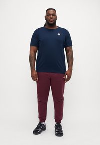 Tricou bleu marin cu mânecă scurtă și un mic logo, asociat cu pantaloni jogger tapered bordo și adidași negri cu accente violet. Material din bumbac fin.