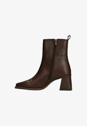 Donkerbruine leren enkellaars met ritssluiting aan de zijkant, blokhak en een lus aan de achterkant, zijaanzicht op witte achtergrond.