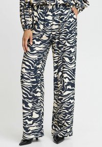 Hlače širokih nogavica s uzorkom zebra u mornarsko plavoj i krem boji, s nabranim detaljima i bočnim džepovima, izrađene od mekanog materijala. Prilagođen kroj i elegantne cipele sa šiljastim nosom.