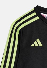 Černé sportovní tričko se zeleným diagonálním designem tří pruhů na rukávech a odpovídajícím vyšitým logem na horní části ramene.