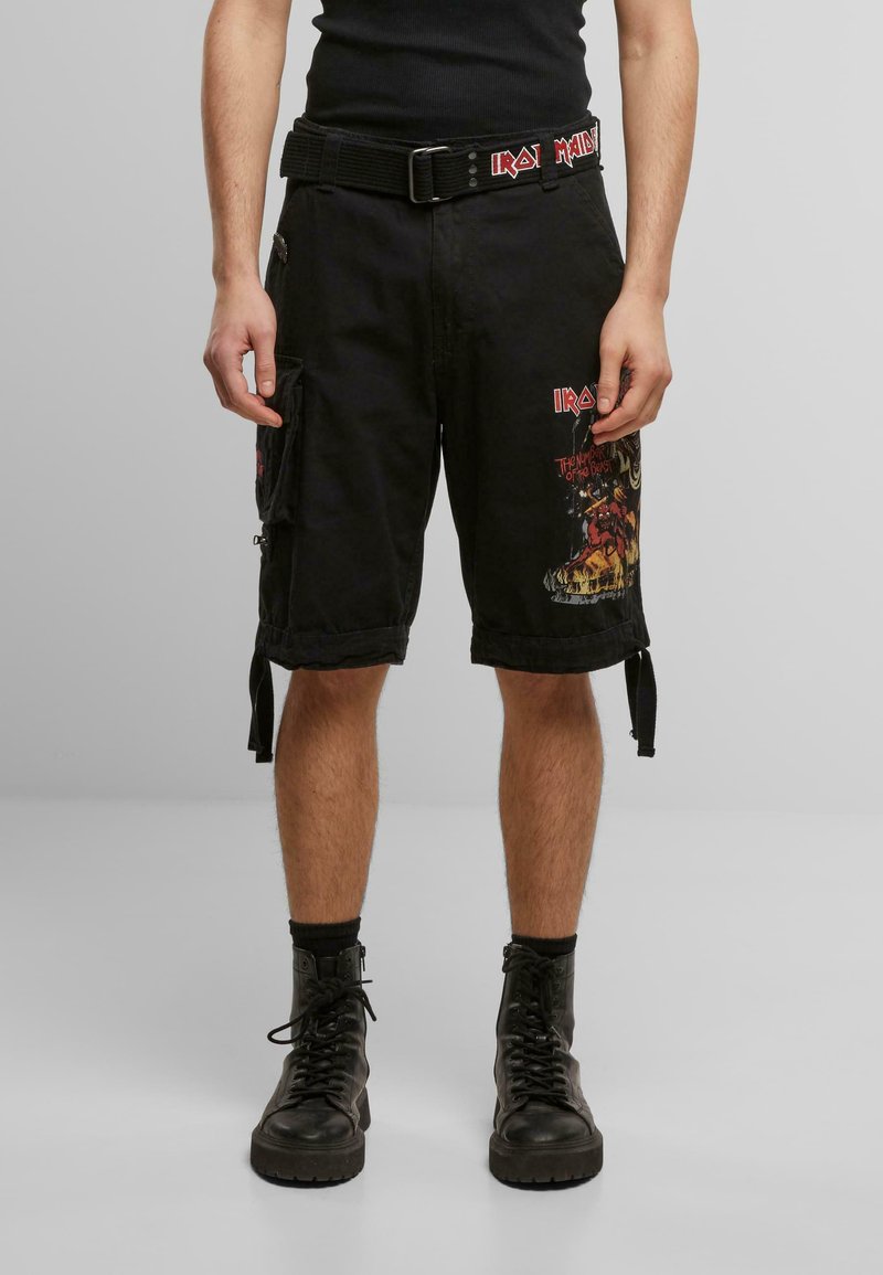 Svarte cargo-shorts med grafiske trykk og logoer, med flere lommer, belte og justerbare sidebelter. Kombinert med svarte militærstøvler.