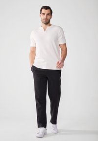 Hvit stripete kortermet polo skjorte med dyp halsringning, kombinert med svarte bukser og hvite sneakers, som skaper et enkelt, moderne utseende.