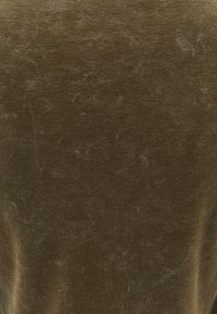 Tela texturizada de color verde oliva con un aspecto aterciopelado. La superficie muestra un brillo sutil y ribetes finos, creando un acabado blando y táctil.