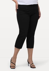 Zwarte capri-broeken van zachte stof, met een slim fit, voorzakken met rits en een zoom die net onder de knie valt. Combineer met zwarte gespenhakken.