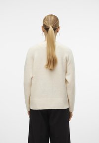 Cremefarvet uldtrøje med afslappet pasform, ribbet kant og lange ærmer. Glat tekstur, med rund halsudskæring og design på ryggen.