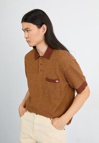 Rudas raštuotas polo marškinėliai su trumpomis rankovėmis, kontrastingas rudas apykaklė, trys mygtukai ir krūtinės kišenė su logotipo detale.