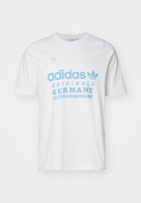 Valkoinen puuvillainen T-paita, jossa siniset "adidas"-tekstit ja logo, "ORIGINALS GERMANY" -painatus sekä raglan-hihat. Sileä pinta.