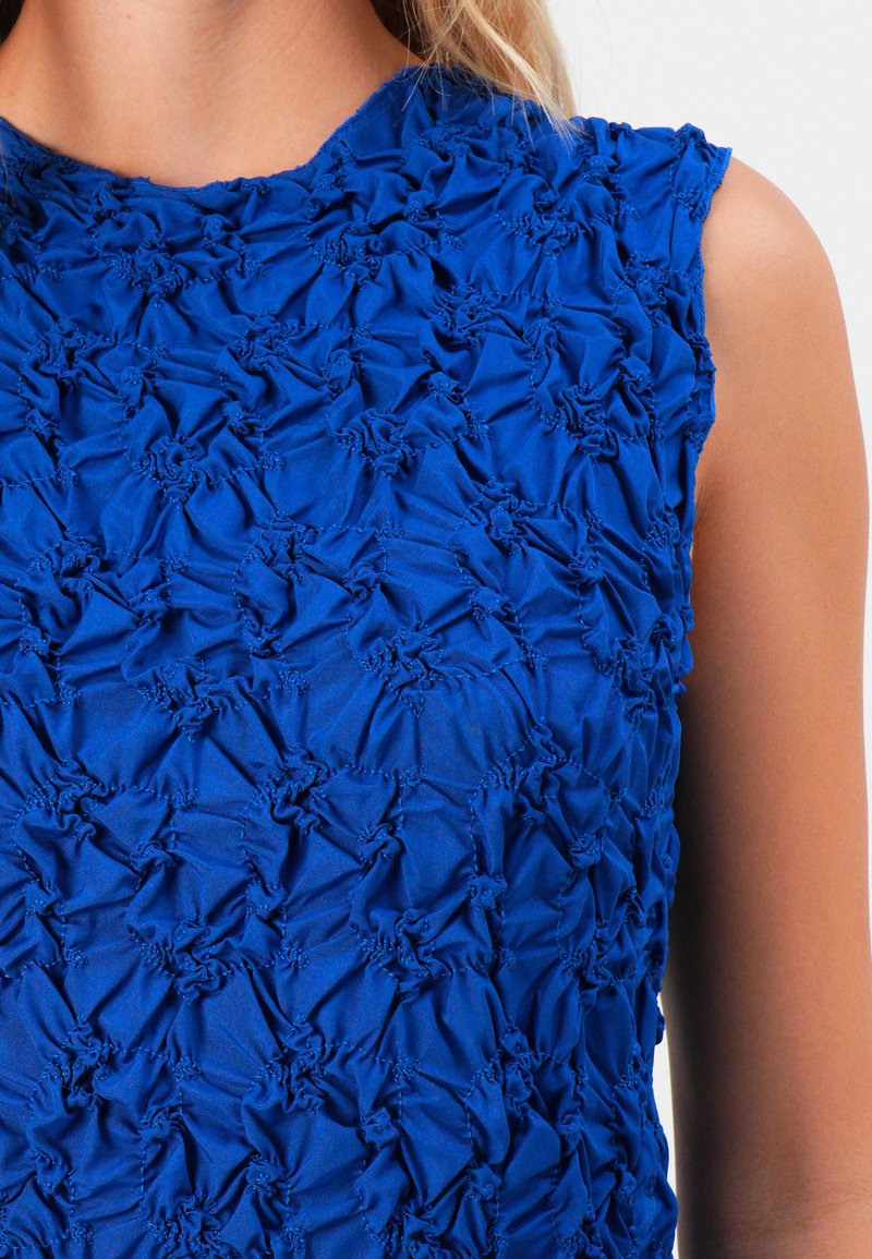 Niebieski top bez rękawów z marszczonym, teksturowanym wykończeniem, które pokrywa klatkę piersiową i obszar ramion.