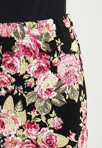 Tissu à imprimé floral avec un fond noir, présentant de grands motifs de roses roses et vertes. Conception de la taille élastique texturée.