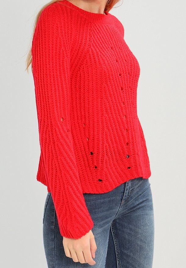 Un pull en tricot rouge avec une texture côtelée, un col rond et de petites découpes. Associé à un jean en denim bleu.