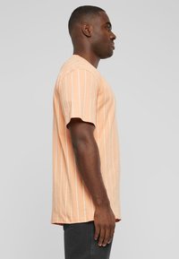 T-shirt à manches courtes, rayé pêche avec des lignes blanches verticales, en tissu coton, coupe décontractée, ourlet arrondi, exposé sur un mannequin de profil.