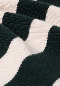 Kangas neulottu, jossa vuorottelevat tummanvihreät ja kermaiset raidat; pehmeä tekstuuri näkyvällä jousto-ompeleella ja vaihteleva langan paksuus.