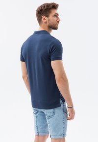 Mörkblå pikétröja i mjuk bomull, med klassisk krage och korta ärmar, kombinerad med ljusa denimshorts.