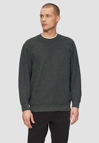 Sweatshirt texturé vert foncé avec un col rond et des poignets côtelés. Présente un petit patch logo près de l'ourlet inférieur.