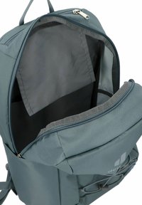 Tümgrüner Rucksack mit geräumigem Innenraum, Reißverschluss und grauer Innenauskleidung. Verfügt über eine Seitentasche und verstellbare Träger für zusätzlichen Komfort.