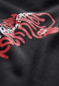 Sort stof med rødt og hvidt abstrakt mønster med flydende former. Teksturen er blød, og det samlede mønster er levende og detaljeret.