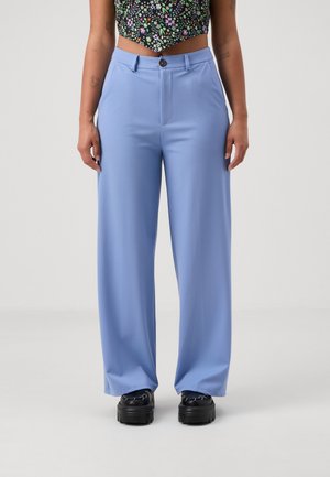 Lichtblauwe wijde broek van een gladde stof, met een sluiting aan de voorkant en een geplooid ontwerp. Gekleed met zwarte plateauschoenen.