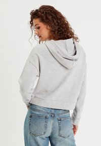 Geknipte grijze hoodie met een trekkoordcapuchon, zachte textuur en geribbelde boorden. Gecombineerd met lichtblauwe jeans met achterzakken.