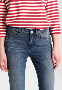 Džínové kalhoty v středně modrém odstínu, s klasickým střihem, pětietízkou a jemným vyblednutím. Zapínání na tlačítko v pase.