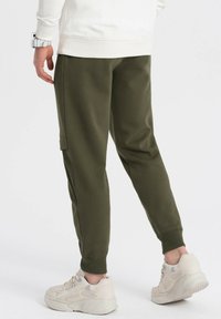 Olijfgroene joggerpants van een zacht materiaal, met taps toelopende pijpen en zijzakken, gecombineerd met lichtbeige sneakers.