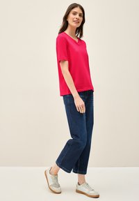 Fuchsia kortærmet V-hals t-shirt kombineret med mørkeblå cropped jeans og lysegrå sneakers med brune såleaftryk.