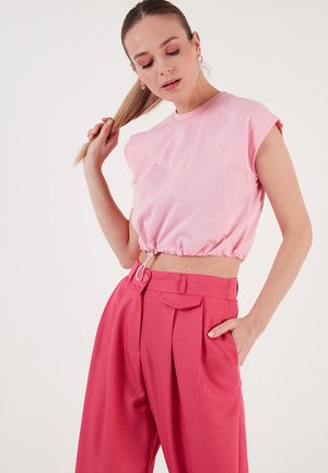 Rosa Cropped T-Shirt mit gerafftem Saum, kurzen Ärmeln, kombiniert mit hochtaillierten rosa Hosen mit Falten und einer Detailtasche auf der Vorderseite.