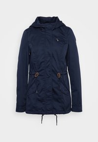 Veste de plein air bleu marine avec une poche poitrine zippée, des cordons de serrage à la taille et deux poches frontales. Fabriquée en tissu léger.