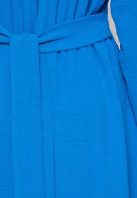 Μπλε φόρεμα με υφή και ζωνάκι στη μέση. Ο σχεδιασμός περιλαμβάνει πτυχώσεις και μακριά μανίκια για άνετη εφαρμογή.