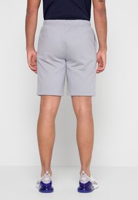 Pantaloncini sportivi grigi con vita elastica, design fino al ginocchio e texture liscia. Indossati con sneakers bianche e viola.