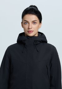 Svart vattentät jacka med dragkedja fram, justerbar huva och slank design. Har sidofickor och minimalistiska detaljer.