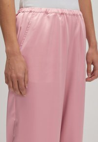 Helles rosa Satin-Hose mit weitem Bein und elastischem Bund; verfügt über Seitentaschen und eine glatte Textur. Nahaufnahme des Kleidungsstücks.