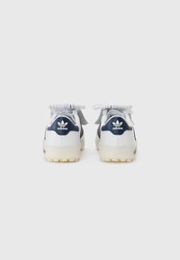 Vita och marinblå sneakers har en texturerad ovandel, rund häl och kontrasterande snören. Logotypen är synlig på hälen och tungan.