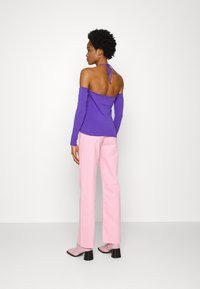 Top longo roxo com decote ombro a ombro e fecho em laço, combinado com calças retas rosa claro e botins de salto rosa.