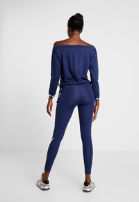 Námořnický top s odhalenými rameny a dlouhými rukávy, kombinovaný s námořnickými legínami s vysokým pasem. Oba kusy mají hladkou, elastickou látku a přiléhavý střih.