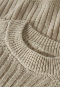 Pull en tricot beige avec une texture côtelée, un col rond et un tissu doux. Détails avec des motifs de côtes horizontales et verticales.