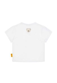 Camiseta blanca de manga corta con un pequeño bordado de la cara de un oso en la parte posterior y una etiqueta de marca amarilla en la costura lateral.