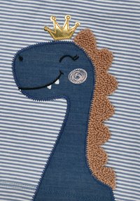 Navyblauer Dinosaurier-Applikation mit einer goldenen Krone, strukturierten braunen Stacheln und gestickten Details, auf einem hellblau-weißen gestreiften Stoff.